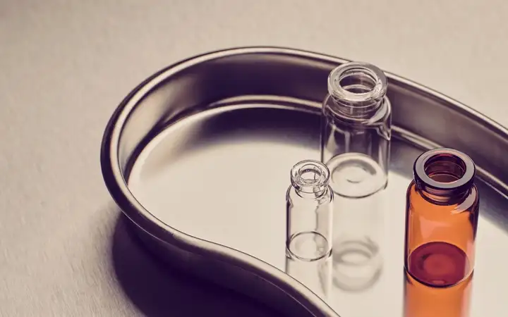 Three small glass vials, one amber and two clear, standing on a stainless steel tray