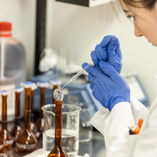 Algalif employee holding pipette over brown jars in the laboratory.