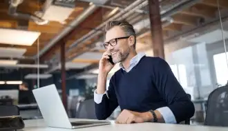 Man in glasses in business office on phone while working on laptop_330x190.jpg