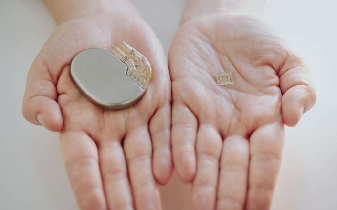 Hands holding large pacemaker and miniaturized implant