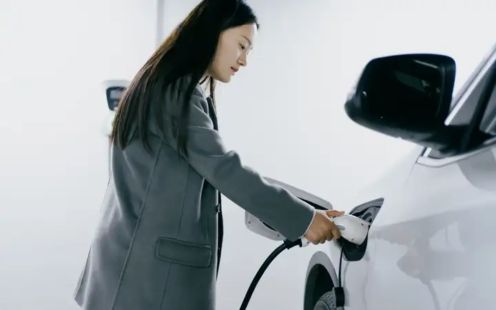 A woman connects a charger to an electric car.