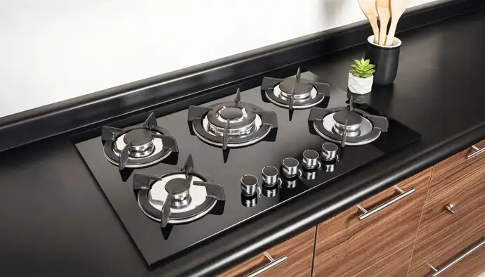 Modern black glass gas cooktop with five burners and stainless steel knobs installed on a sleek black countertop.