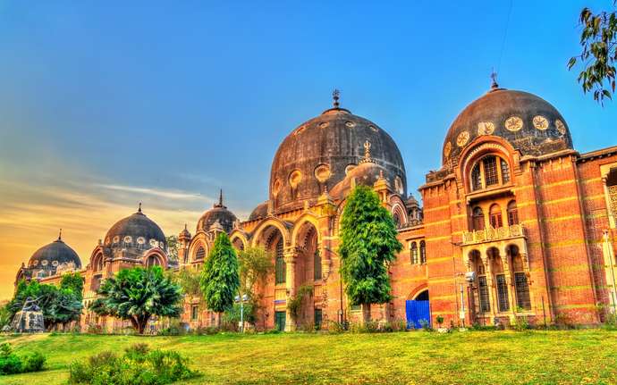 Historic Maharaja Sayajirao University building in Vadodara, India, with domes and red brick at sunset.