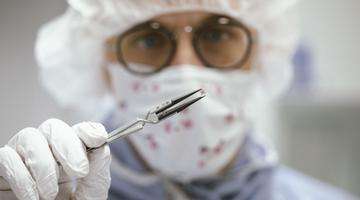 Photo of a laboratory employee who holds a miniaturized medical implant with tweezers