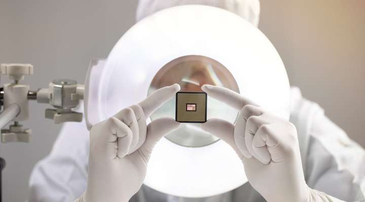 Person in cleanroom holding a microchip wafer in front of a circular inspection light