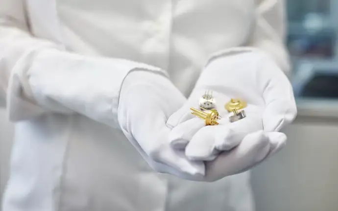 身穿实验室工作服的人员手持玻璃-金属密封技术生产的电子元件。 