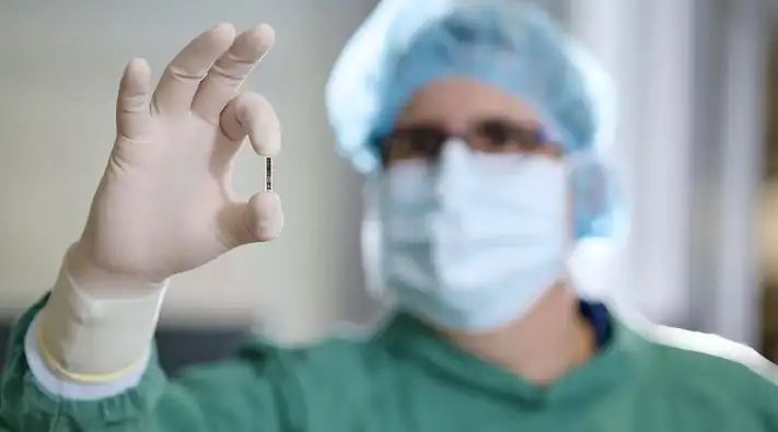 A doctor clad in surgical gowns holds Kitea Health's tiny sensor between his thumb and forefinger.