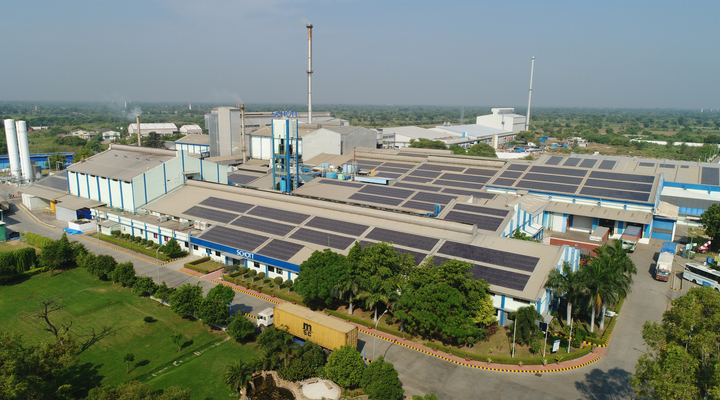 Aerial view of a SCHOTT production facility with solar panels, surrounded by greenery and industry.