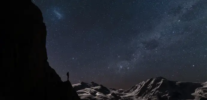 Person standing in a desert landscape front of a night-sky full of stars