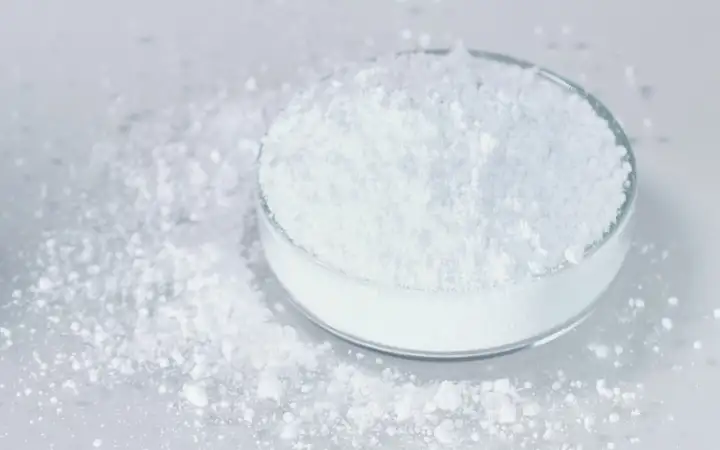 White glass-ceramic powder in a petri dish, with some spilled on a grey surface.