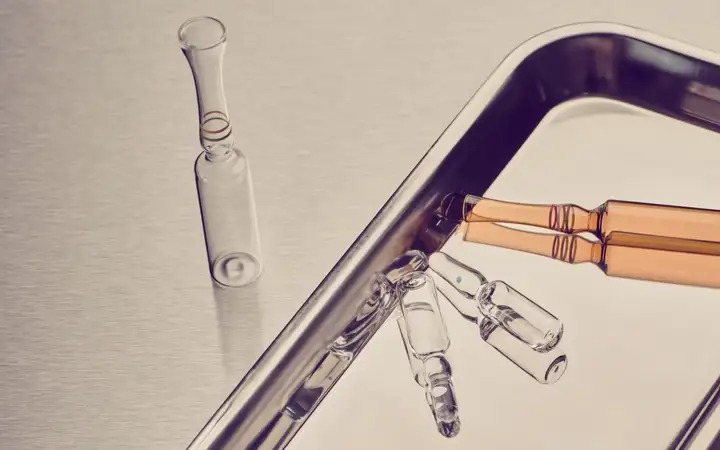Glass ampoules, including two amber ones, arranged on a metal medical tray