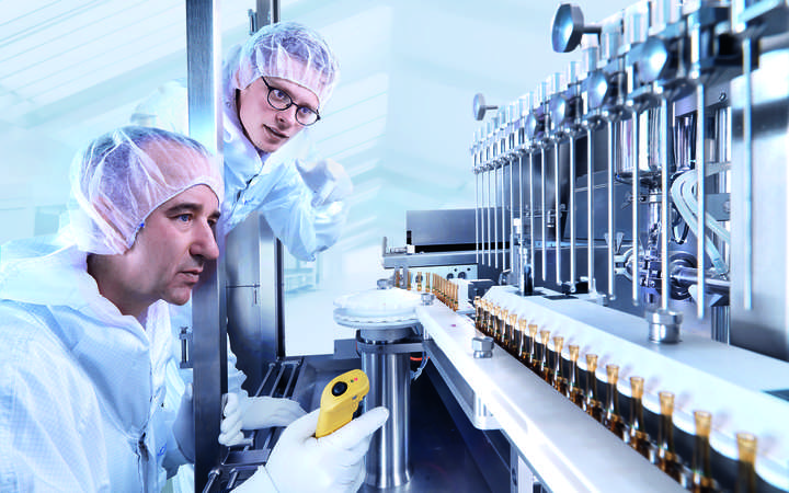 Two scientists looking at glass processing equipment producing ampoules