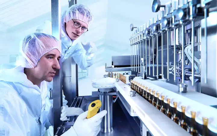 Two scientists looking at glass processing equipment producing ampoules