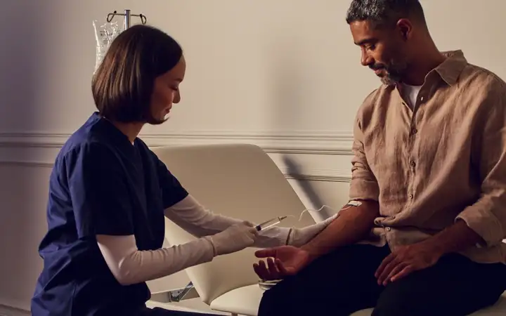 Healthcare worker drawing blood from a seated man's arm in a clinic exam room
