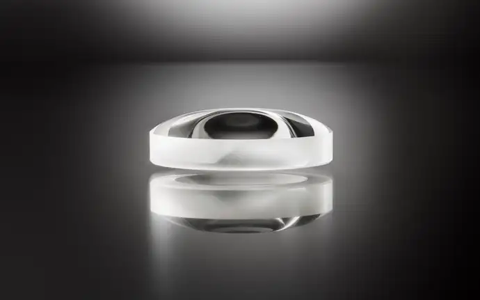 Single, clear aspherical lens by SCHOTT on a dark background with reflections on its surface