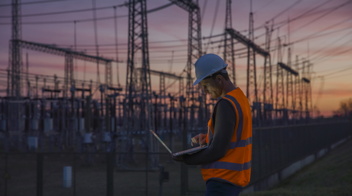 Person in high-visibility vest using a laptop at an electrical substation