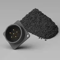 A black electrical connector with gold pins placed next to a pile of black granular material on a gray background.