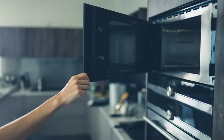Young woman opening a microwave door