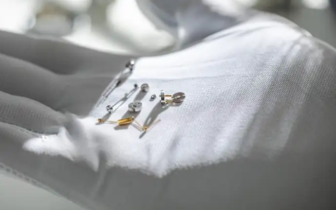 A close-up of tiny implantable feedthroughs and battery lids resting on a white gloved hand, captured under soft lighting to highlight their intricate details and craftsmanship.