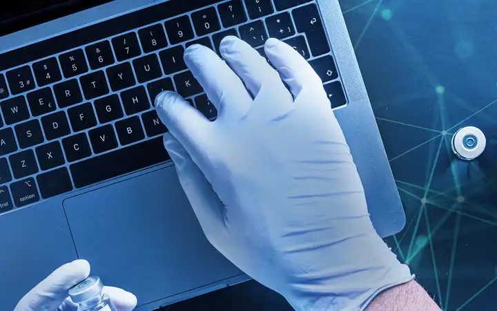 Person sitting in front of laptop with vial in hand