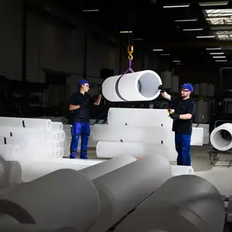 Two workers standing between large industrial pipes inside a quartz glass production facility.