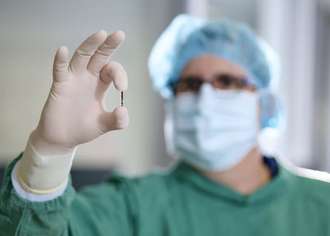 A doctor clad in surgical gowns holds a small sensor between his thumb and forefinger.