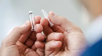 手里拿着两个笔帽大小的玻璃药品包装