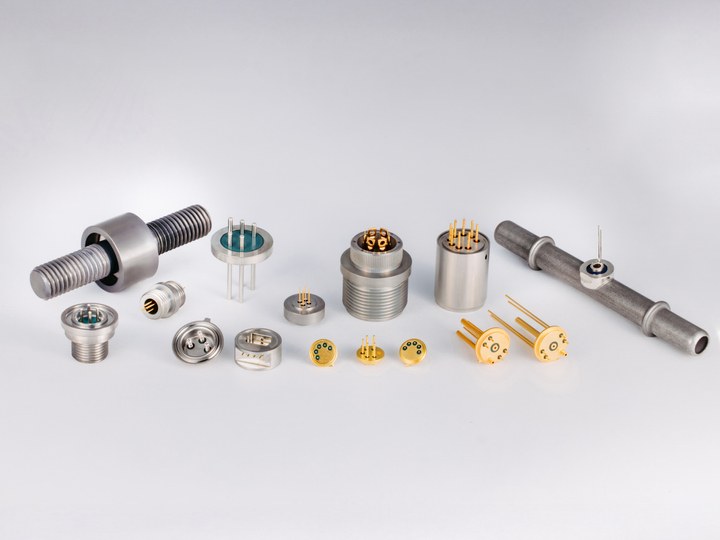 Close-up of gold-plated sensor feedthroughs with pins on a clean white surface.